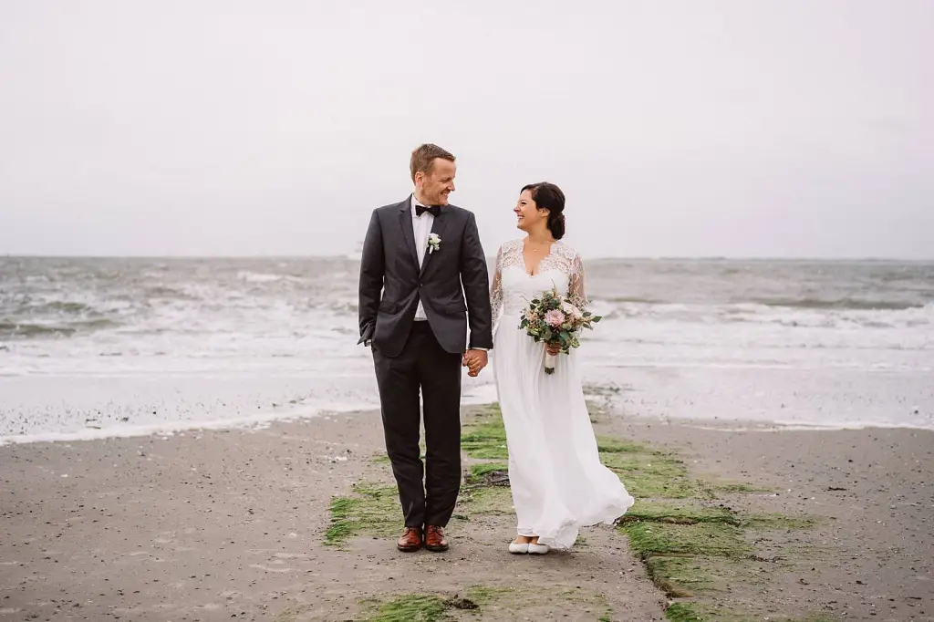Hochzeitspaar spaziert Hand in Hand am Meer auf Norderney nach der Trauung in der Hochtiedsstuv