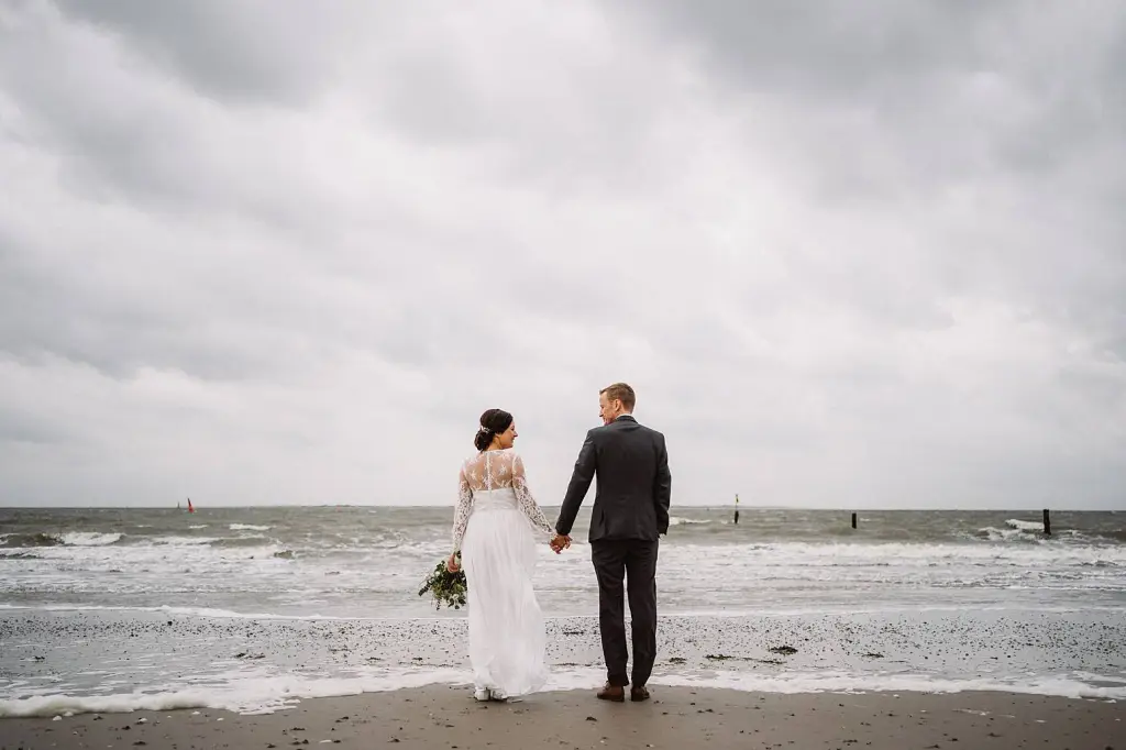 Hochzeitsfotograf Norderney – Brautpaar Hand in Hand am Strand bei Sonnenlicht