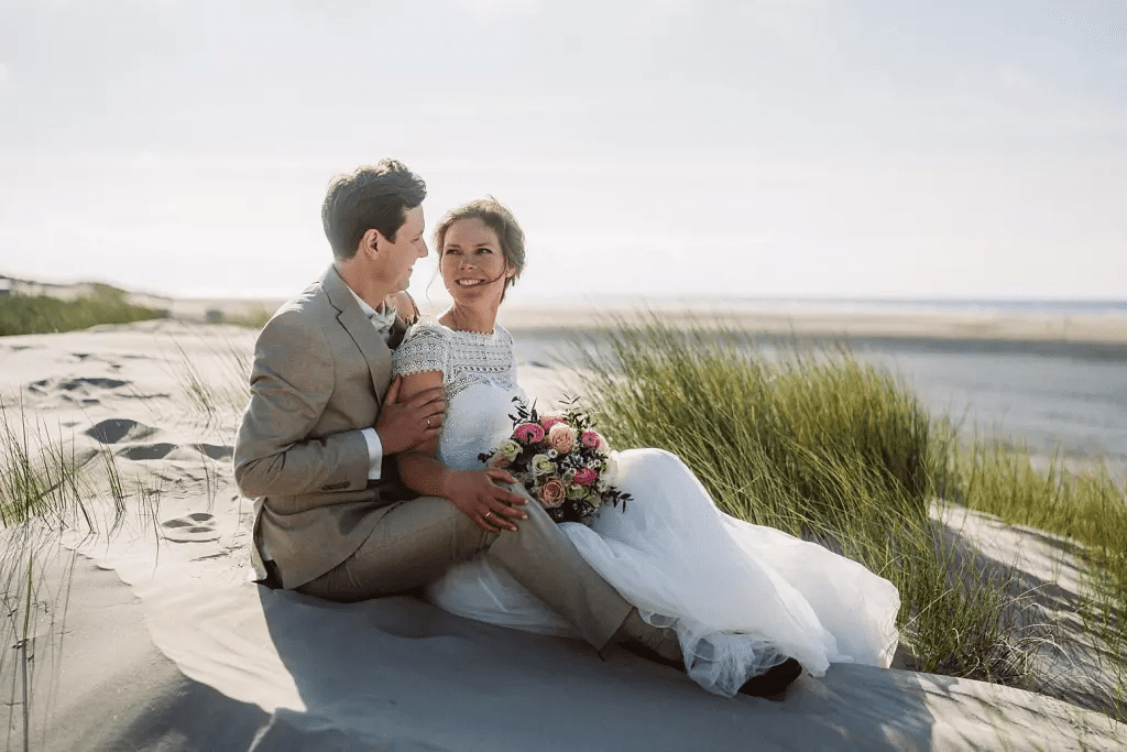 Brautpaar sitzt in den Dünen von Juist – ruhiges Hochzeitsfoto mit Blick auf Strandhafer und Nordsee