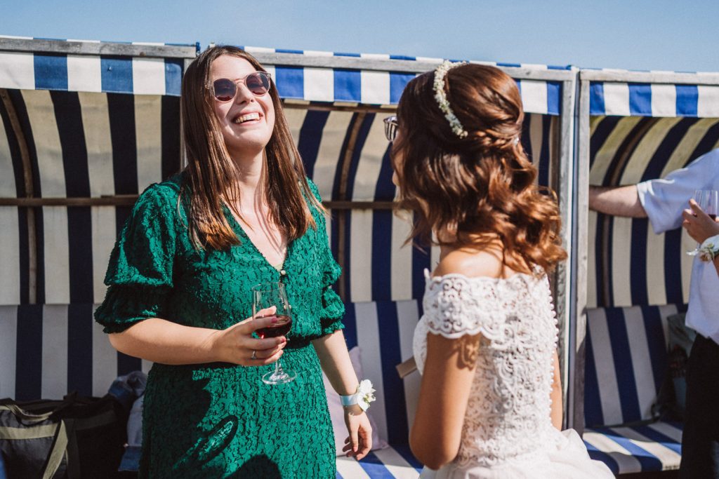 Braut im Gespräch mit Hochzeitsgast am Strand von Norderney vor dem Badekarren