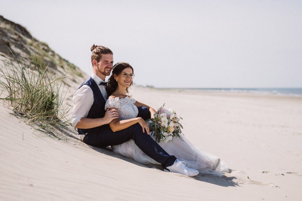 Hochzeitspaar sitzt verliebt in den Dünen am Strand von Norderney beim Fotoshooting