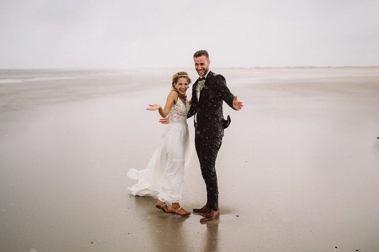 Brautpaar lacht im strömenden Regen am Strand von Norderney – emotionale, natürliche Hochzeitsfotos.