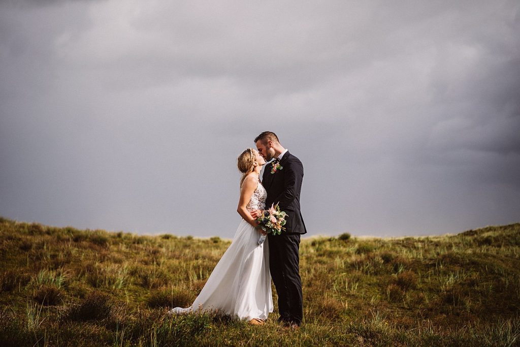 Hochzeitsshooting in den Dünen am Nordstrand von Norderney, romantischer Kuss unter dramatischem Himmel.
