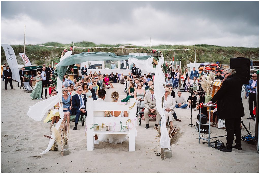 Freie Trauung am Strand von Baltrum mit Blick auf Dünen und Nordsee – Brautpaar sitzt vor dem Traubogen, Hochzeitsgäste verfolgen die Zeremonie auf der ostfriesischen Insel