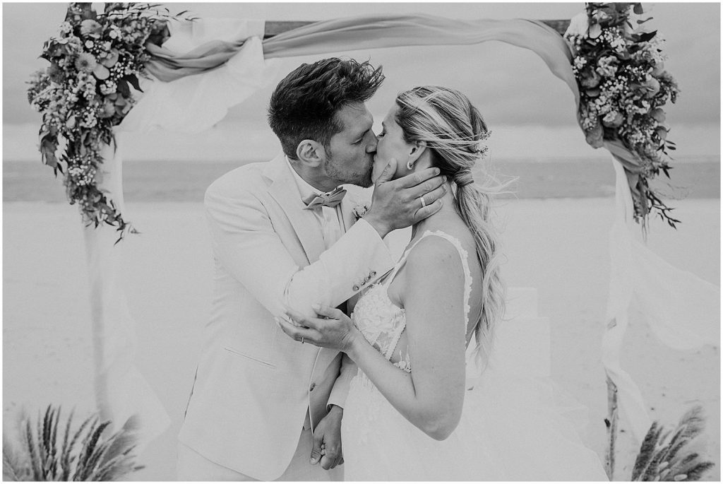 Brautpaar küsst sich nach dem Ja-Wort unter dem Traubogen am Strand von Baltrum – emotionale Hochzeitsreportage bei freier Trauung auf der ostfriesischen Insel