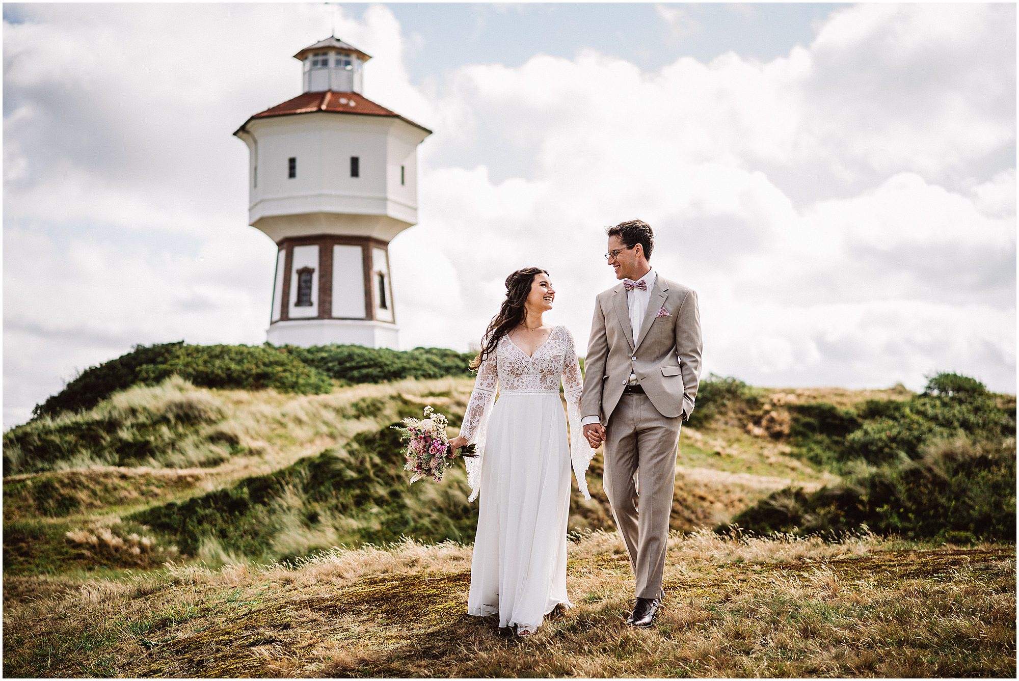 Brautpaar geht Hand in Hand bei am Wasserturm auf Langeoog in den Dünen