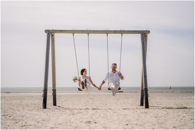 Braut und Bräutigam lachen am auf einer Schaukel am Strand bei einer Inselhochzeit auf Norderney